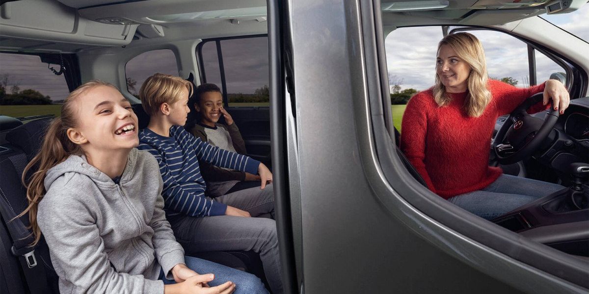 Maman dans sa Toyota Proace City Verso qui regarde ses trois enfants à l'arrière rassurée parce qu'elle a une bonne assurance auto