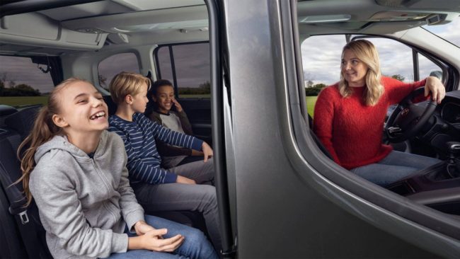 Maman dans sa Toyota Proace City Verso qui regarde ses trois enfants à l'arrière rassurée parce qu'elle a une bonne assurance auto