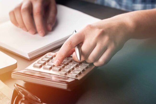 Homme assis à un bureau avec un cahier ouvert et une calculette en train de calculer la fiscalité de sa voiture de société