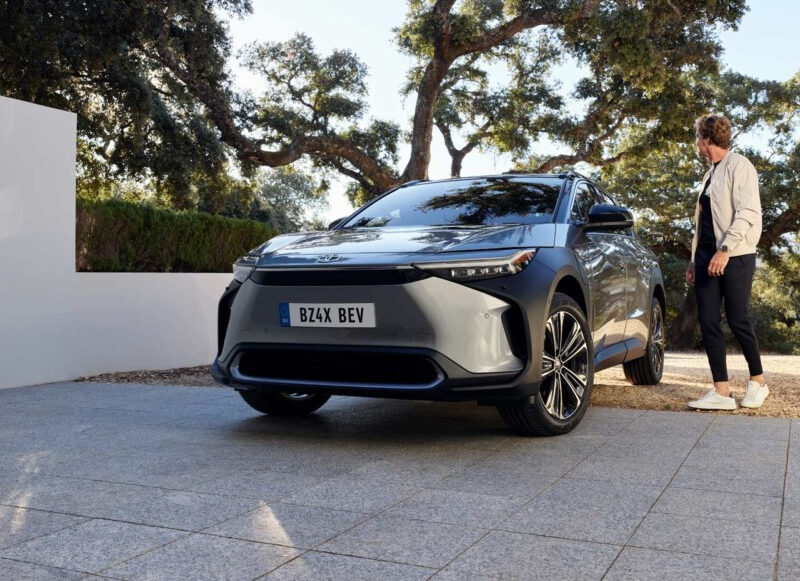 Toyota BZ4X grise garée sur la coure d'une maison avec un homme montant dans le siège conducteur